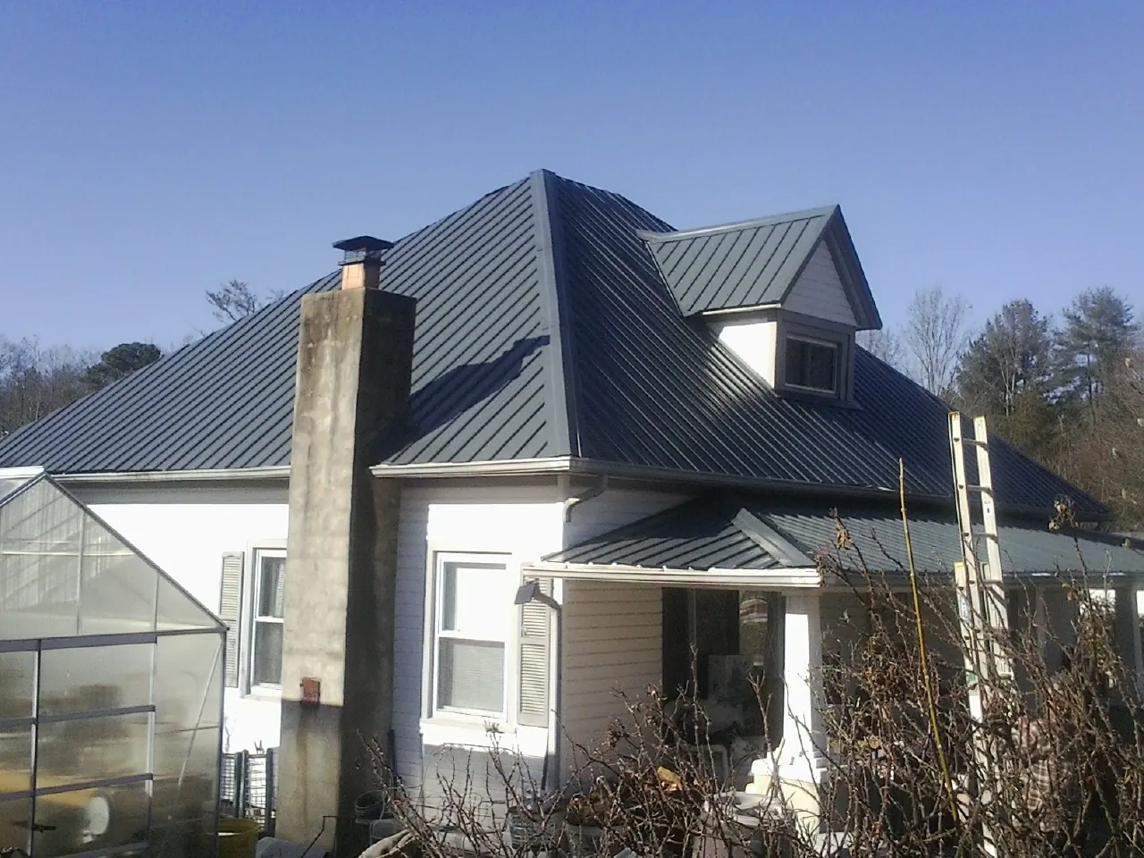 Dark blue standing seam metal roof on a white farmhouse with dormer — Slate & Tile Roof Repair by Roofing Brothers in Blencoe