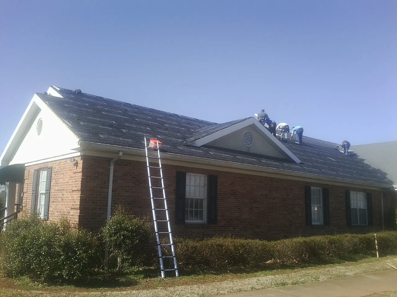 Crew tearing shingles off a brick ranch roof with a ladder set — Metal Roof Repair work by our crew in Blencoe