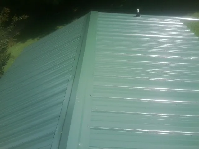 New green metal panels meeting at the ridge of a roof — Flat Roof Repair work by our crew in Blencoe
