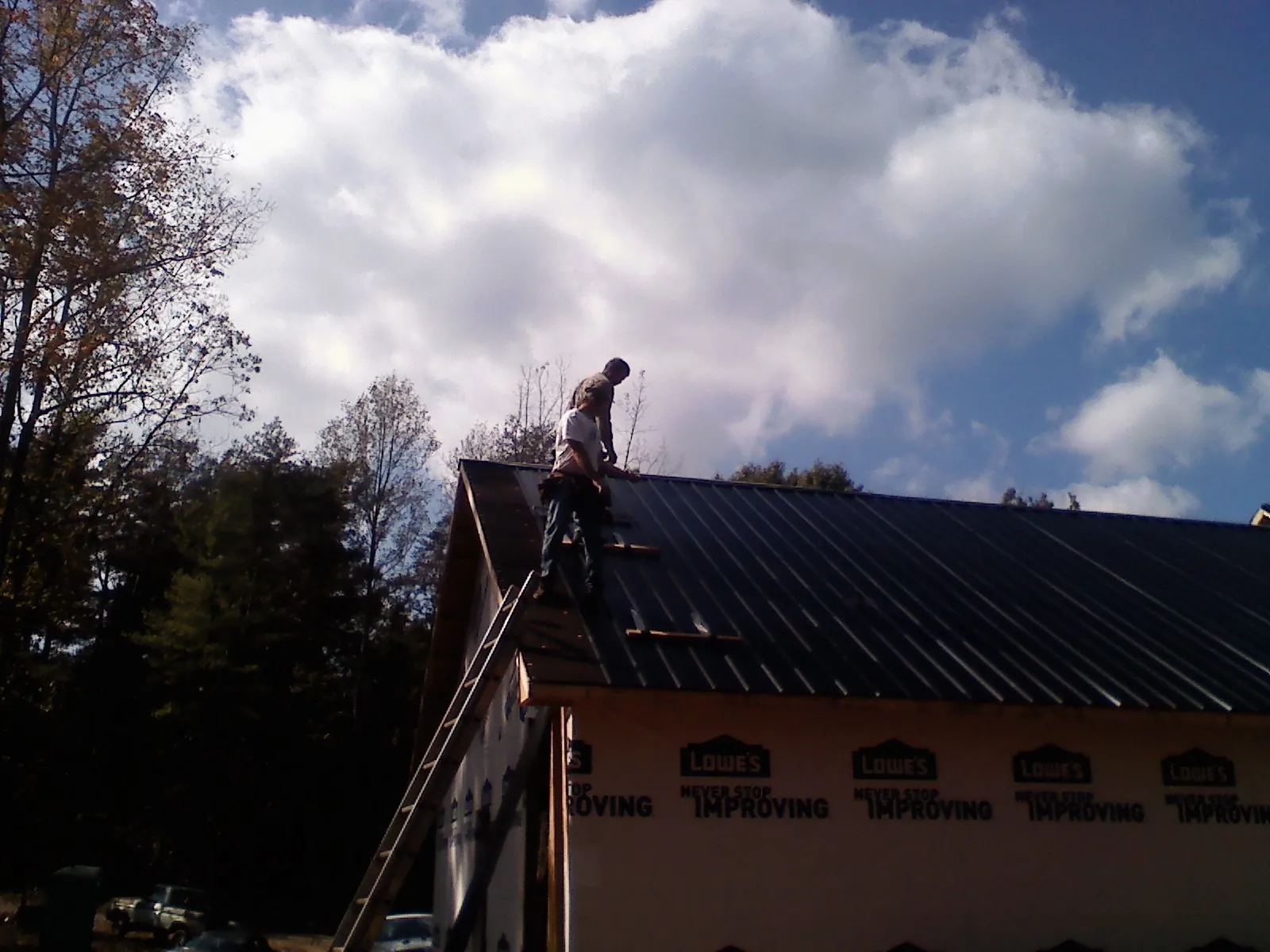 Roofer fastening dark metal panels high against a cloudy sky, from a Roof Inspection job in Blencoe