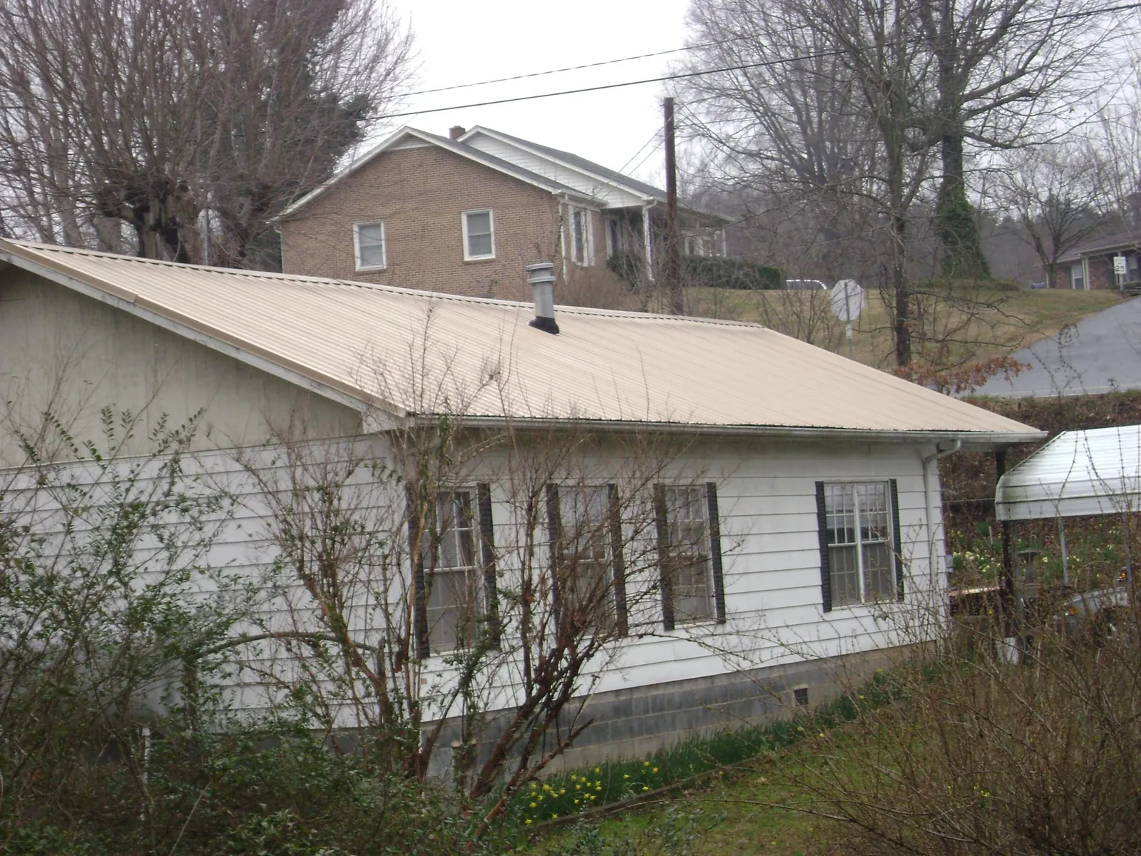 Tan metal roof on a white sided house set into a hillside — Commercial Roofing by Roofing Brothers in Blencoe