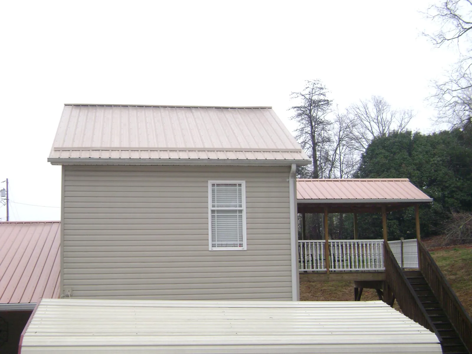 Tan metal roofs on a two story addition and attached porch, from a Roof Replacement job in Blencoe